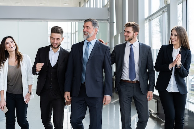 Squadra di persone di affari che cammina in ufficio moderno con leader maturo in primo piano