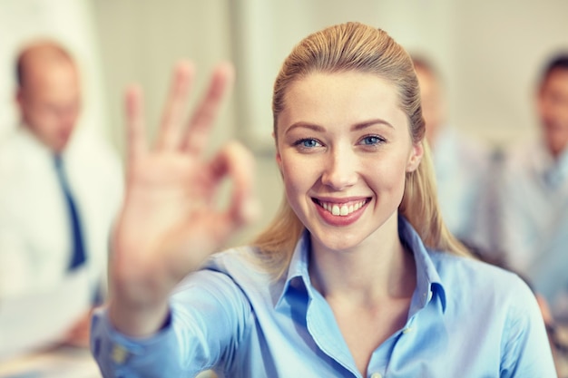 Foto concetto di affari, persone e lavoro di squadra - imprenditrice sorridente che mostra il gesto giusto con un gruppo di uomini d'affari che si incontrano in ufficio