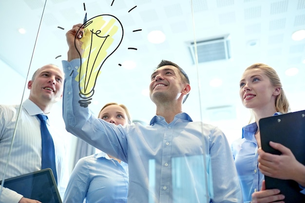 Foto concetto di business, persone, lavoro di squadra e pianificazione - team di affari sorridente con pennarello e lampadina doodle che lavora in ufficio