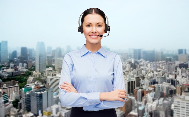 business, people, technology and communication concept - happy female helpline operator in headset over city background