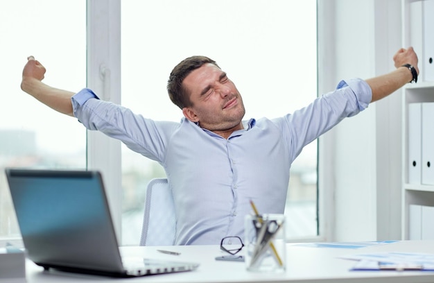 business, people and technology concept - bored businessman with laptop computer and papers at office