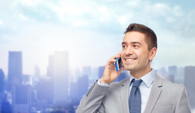 business, people and technology concept -happy businessman calling on smartphone over city background