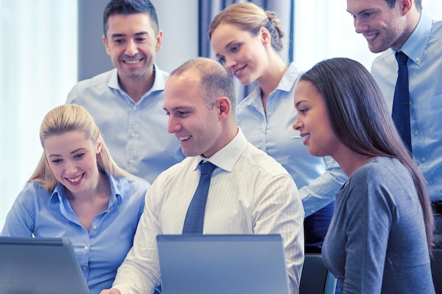 business, people and technology concept - smiling business team with laptop computer meeting in office