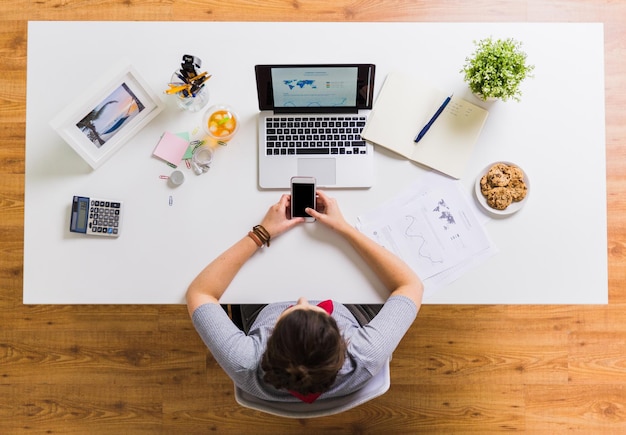 концепция бизнеса, людей и технологий - женщина со смартфоном и ноутбуком за офисным столом