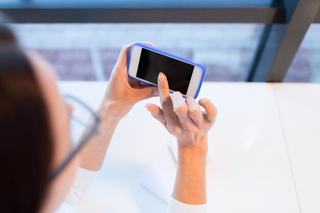 Foto concetto di business, persone, tecnologia e stile di vita - primo piano di una giovane donna in occhiali che invia messaggi di testo con lo smartphone in ufficio