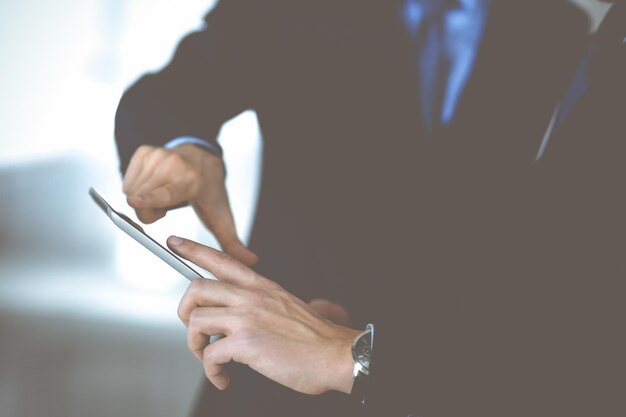 Business people use a tablet computer for discussion of their new project, standing in a modern office. Unknown businessman or male entrepreneur with a colleague at workplace. Teamwork and partnership