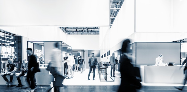 Business people walking between trade show booths at a public
event exhibition hall, with banner and copy space for individual
text