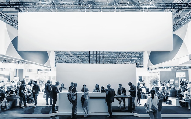 Business people walking between trade show booths at a public event exhibition hall with banner and copy space for individual text