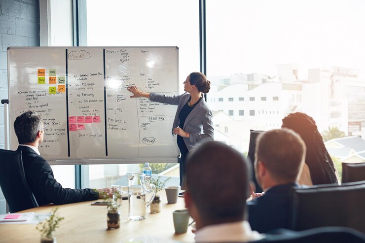 Photo business people whiteboard and woman speaker with presentation in office for planning schedule or project management leadership coaching and manager hand pointing to objectives note or priority