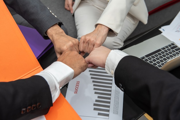 Business people with fist bump together in teamwork at the office above desk with document.