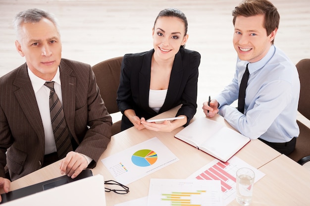 Photo business people at work. top view of three confident business people in formalwear working together while sitting together at the table and smiling