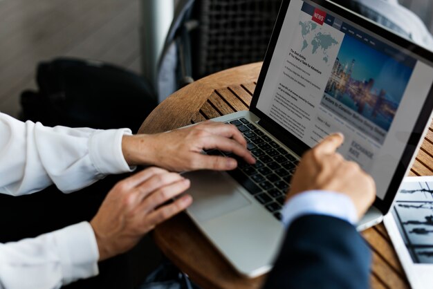 Business people working on a laptop with news coverage on the screen