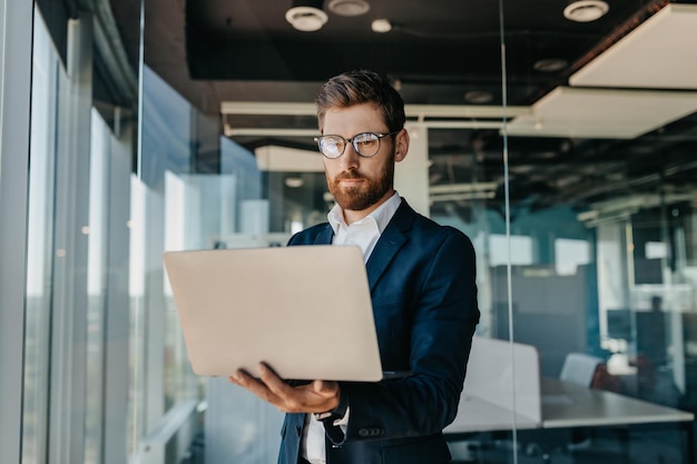 Business person Successful middle aged businessman with laptop in hands standing in modern office interior