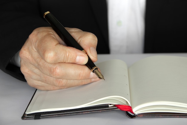 Business person writing with a pen on a notepad.