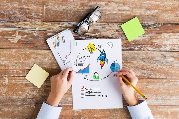 business, planning, startup, management and people concept - close up of female hands writing on paper with scheme and eyeglasses on table