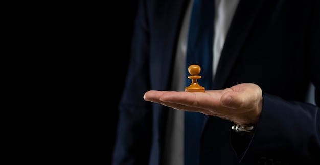 Business planning strategy and concept. A businessman in a dark suit holds a white chess pawn on a scaly background. Strategy and tactics.