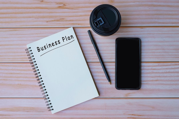 Business plant text on notepad with pen coffee and smartphone on wooden table Space for text