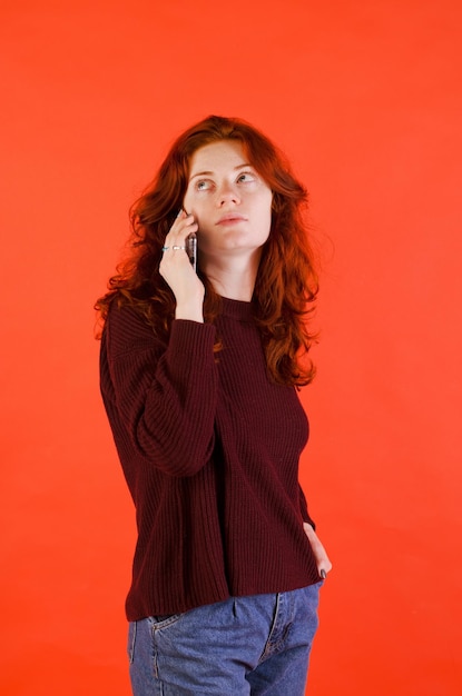 Business portrait of beautiful young woman. red curly hair and blue eyes. red background. Phone