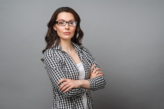 Business portrait of a young woman a charming brunette with glasses looks at the camera crossing her