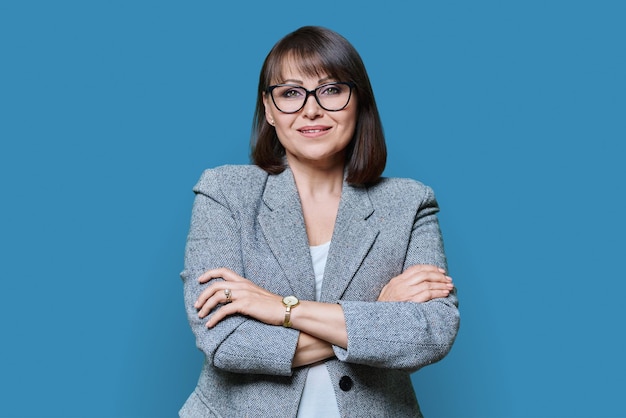 Business positive middle age woman with arms crossed on blue background