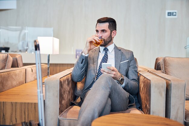 Business professional swallowing some whisky while working on a phone