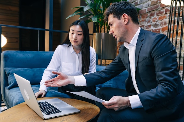 Business professionals are sitting at a table and looking at a laptop