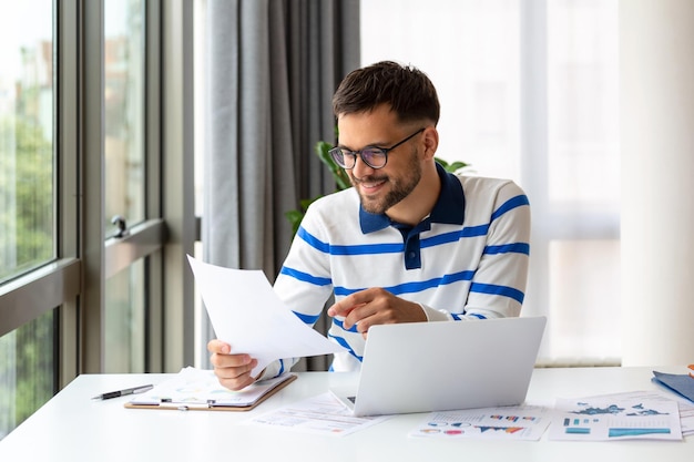 Business professionals Business man analyzing data using computer while spending time in the office Young grinning professional man in office Graphs and charts