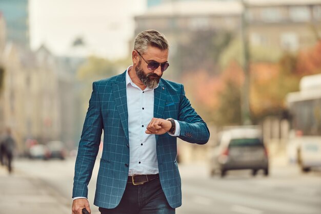 business, punctuality and people concept - senior businessman checking time on wristwatch or smart watch on his hand in city.