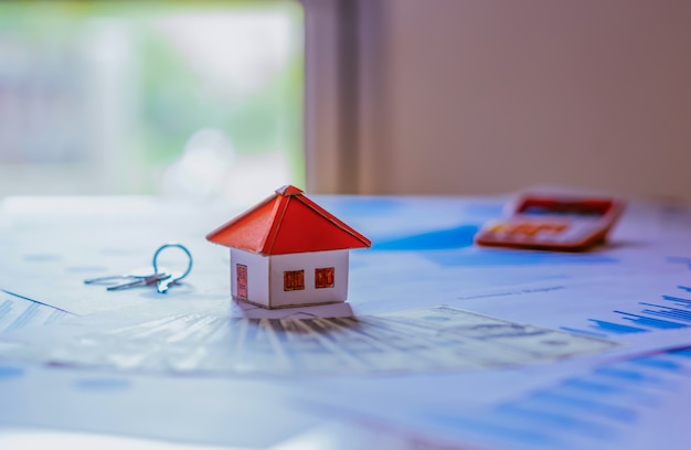 Business Real Estate Concept, House model with a key and dollar bills put on paper graph on wooden background.