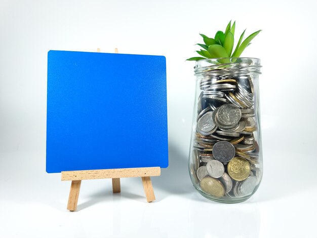 Business saving conceptblank wooden board for textglass\
jargreen plant and coins isolated