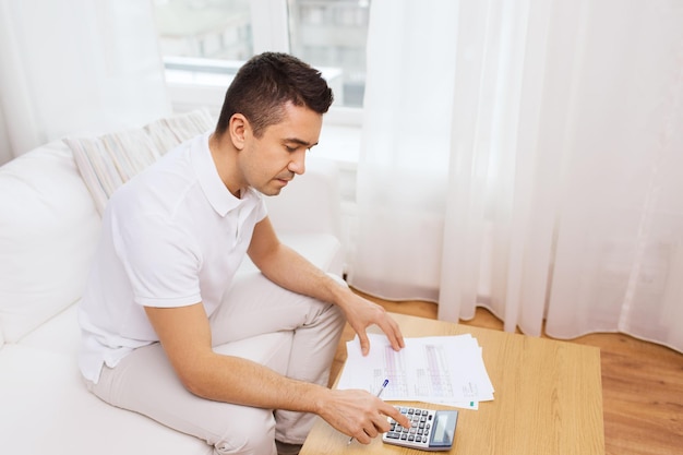 business, savings, finances and people concept - man with papers and calculator at home counting and filling tax form