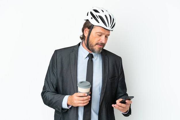 持ち帰り用のコーヒーと携帯電話を保持している白い背景で隔離の自転車のヘルメットを持つビジネスシニア男性