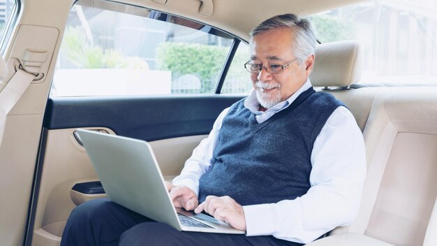 Business senior rich man Stock trader player in suit working with laptop computer and using a smart phone in his car concept for senior business success