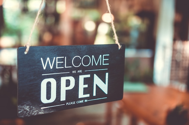 A business sign that says open on cafe or restaurant hang on door at entrance.