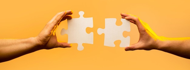 Foto soluzioni aziendali, successo e concetto di strategia. due mani che cercano di collegare un paio di pezzi di puzzle su sfondo giallo. tenendo puzzle. concetto di lavoro di squadra