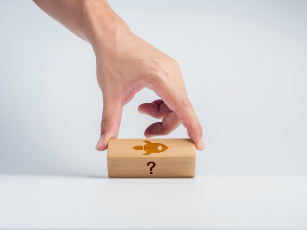 Business startup concept. The man's hand flipping wooden block with question mark icon change to rocket symbol on white background. Problem and solution. The unique business idea among failing ideas.