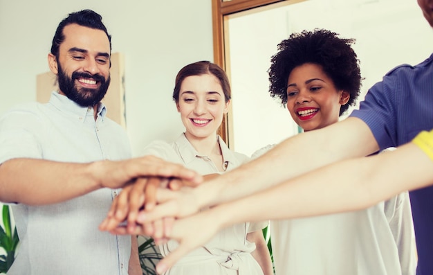 Photo business, startup, gesture, people and teamwork concept - happy creative team with hands on top of each other in office