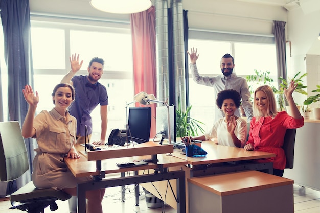 Photo business, startup and office concept - happy creative team waving hands in office