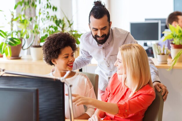 Photo business, startup and people concept - happy creative team with computer discussing something in office