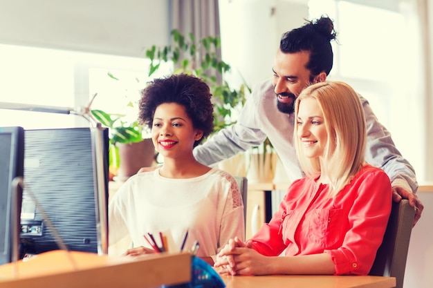 business, startup and people concept - happy creative team with computer discussing something in office