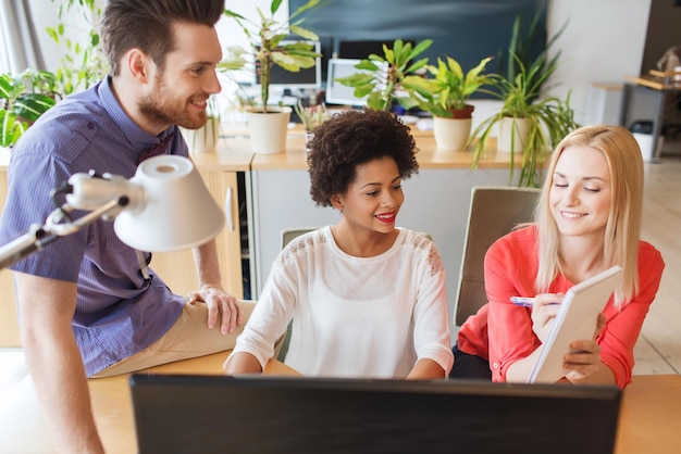 business, startup and people concept - happy creative team with computer and notebook in office