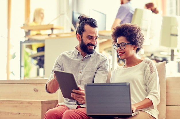 business, startup and people concept - happy creative team with laptop and tablet pc computer in office