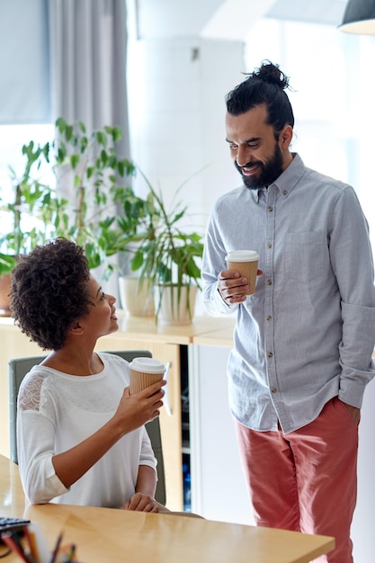 business, startup, people and drinks concept - happy latin man and african woman drinking coffee and talking in office