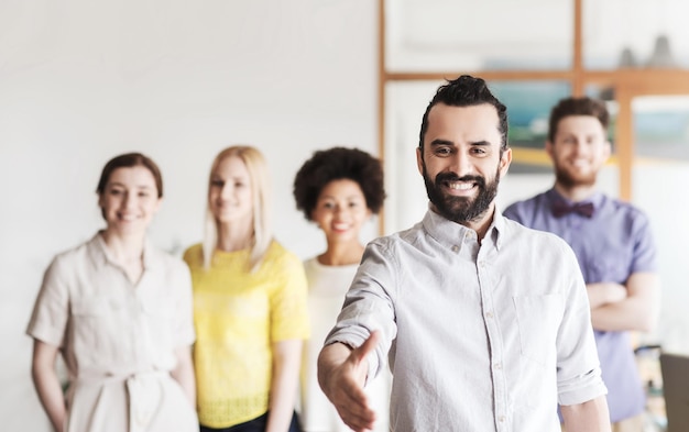 Foto concetto di business, startup, persone, gesti e lavoro di squadra - giovane felice con la barba che saluta con la stretta di mano sul team creativo in ufficio