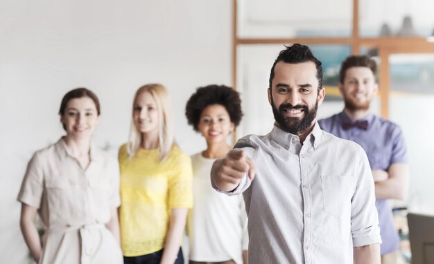 Foto business, startup, persone, gesto e concetto di lavoro di squadra - giovane felice con la barba che ti indica con il dito sulla squadra creativa in ufficio