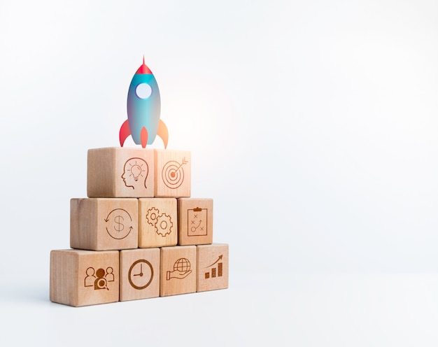 Business startup with growth success process for Leadership concept. The rocket on the top of wooden cube blocks as a stair step with up arrow sign strategy icon on white background with copy space.