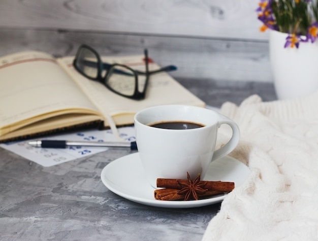 Business still life with cup of black coffee, notebook, pen, glasses on grey concrete table