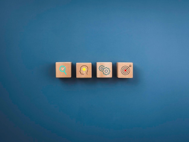 Business strategy and action plan concept. Four wooden cube blocks with business strategy icon symbols on a blue background, top view, minimal style.