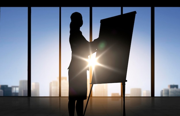 business, strategy, planning and people concept - silhouette of woman with flipboard over office window background