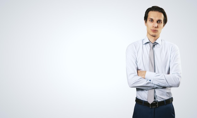 Business success concept with young smiling businessman folding his hands in white shirt and dark blue trousers on abstract light blank background with place for your logo or text Mock up